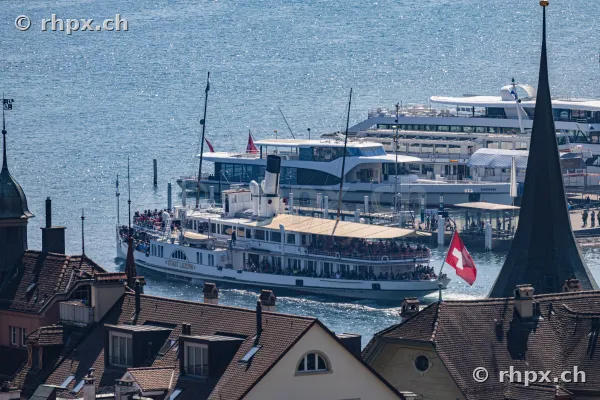 The paddle steamer Stadt Luzern sails in front of the old town rooftops on Lake Lucerne.