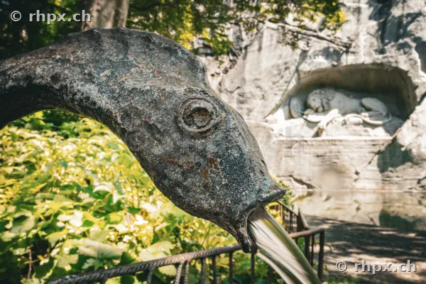 Close-up of a stone fountain head with the Lion Monument in Lucerne in the background