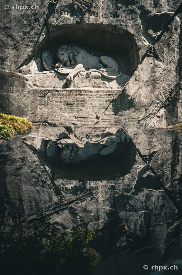 Das in den Fels gehauene Löwendenkmal in Luzern spiegelt sich in der Wasserfläche.