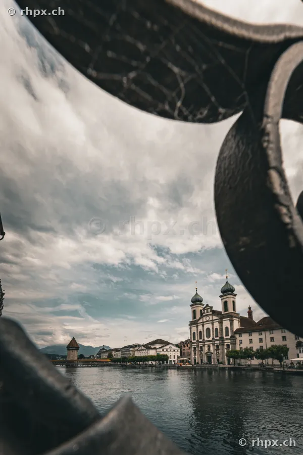 Blick durch ein eisernes Geländer auf die Jesuitenkirche und den Wasserturm in Luzern an der Reuss.