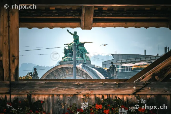 View through the wooden roof structure of the Chapel Bridge to the sculpture at Lucerne Station