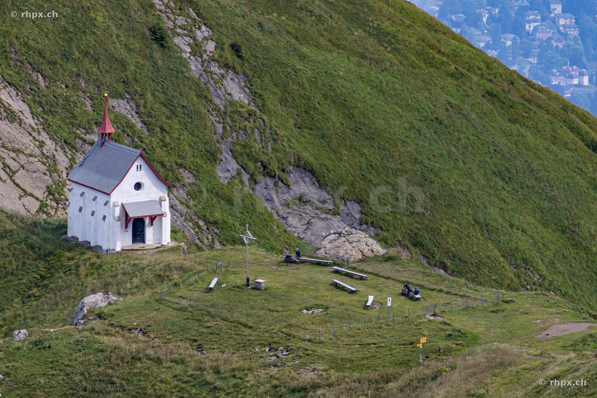 White chapel on the grassy slope of Mount Pilatus with hikers