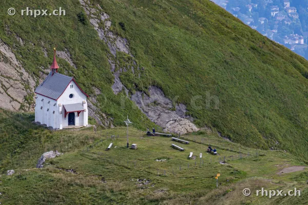 Weisse Kapelle am grasbewachsenen Hang des Pilatus mit Wanderern