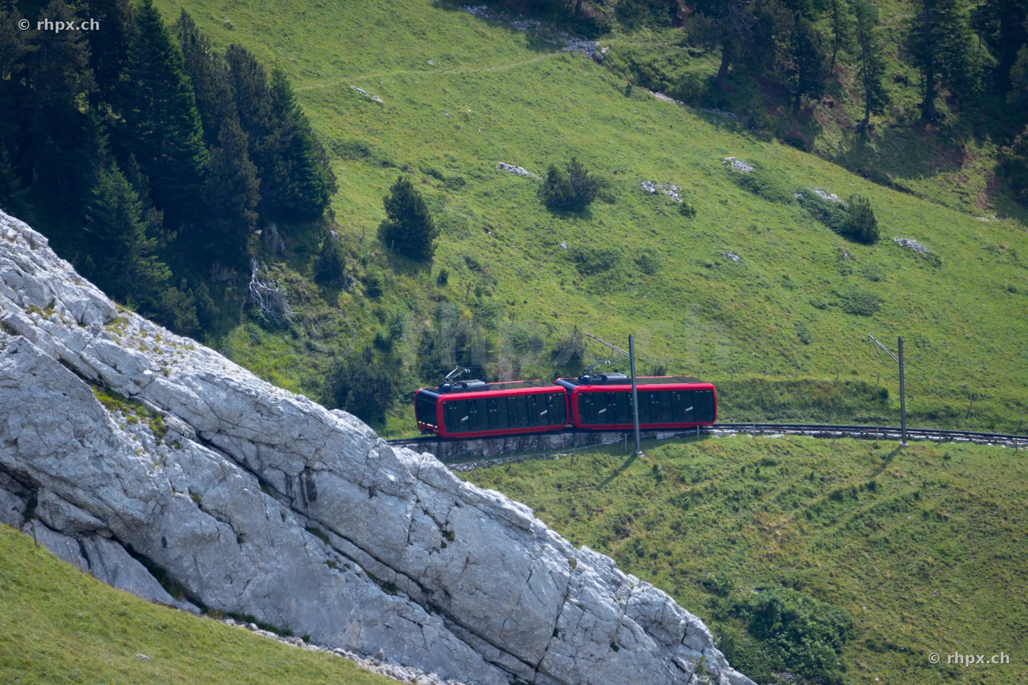 Red cogwheel train on the Pilatus mountain moving along a rocky slope and green meadows