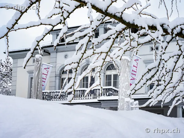 Die verschneite Fassade der Villa Schweizerhof in Luzern mit schneebedeckten Ästen im Vordergrund