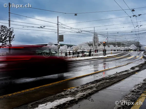 Bahnhofplatz Luzern mit verschneiten Bäumen und einer roten Bewegungsunschärfe eines Fahrzeugs bei trübem Wetter