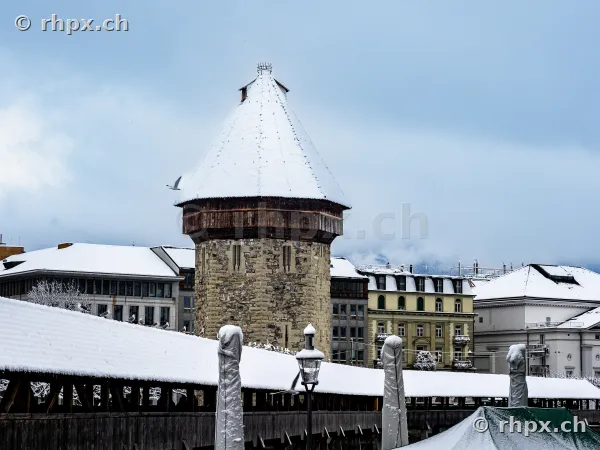 Snow-covered water tower at the Chapel Bridge in Lucerne under a cloudy sky