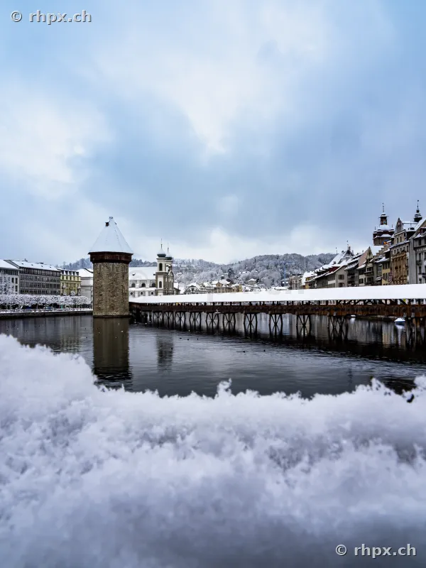 Snow-covered Chapel Bridge with Water Tower in Lucerne on a winter day