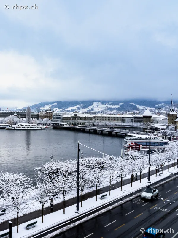 Blick über das verschneite Luzerner Seebecken und das Hotel Schweizerhof bei bewölktem Himmel