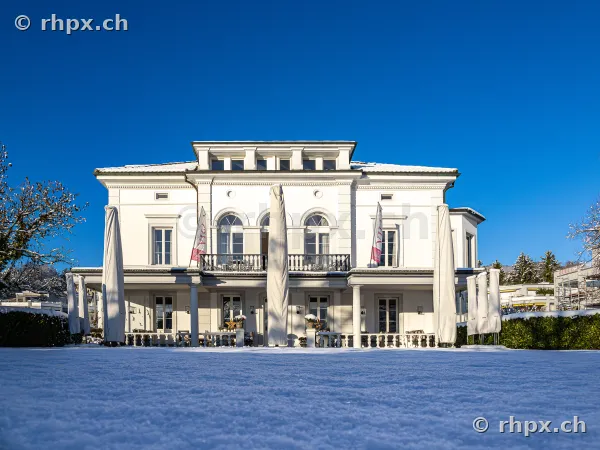 Weisse Villa Schweizerhof in Luzern vor blauem Himmel in verschneiter Parklandschaft