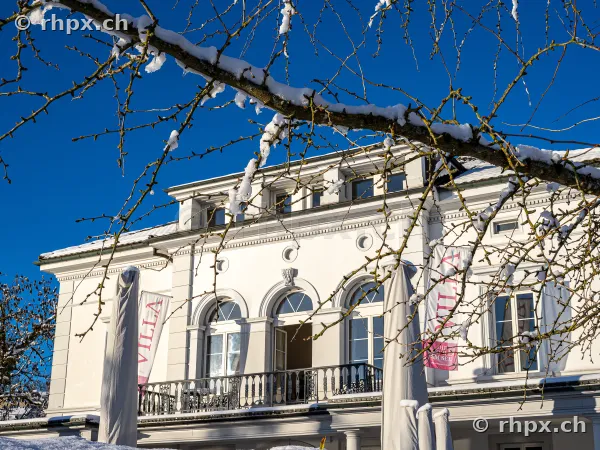 Fassade der Villa Schweizerhof in Luzern bei klarem Winterwetter mit verschneiten Ästen im Vordergrund