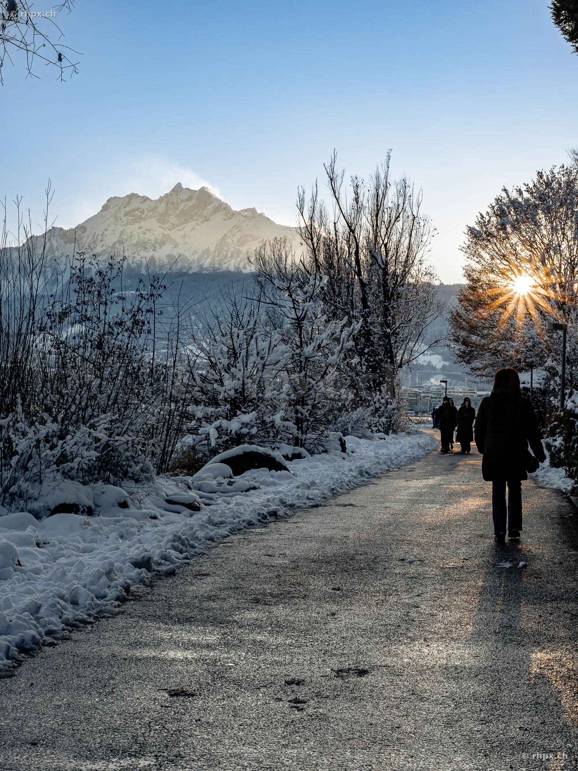 People walking on a snowy path with a view of the sunny Mount Pilatus