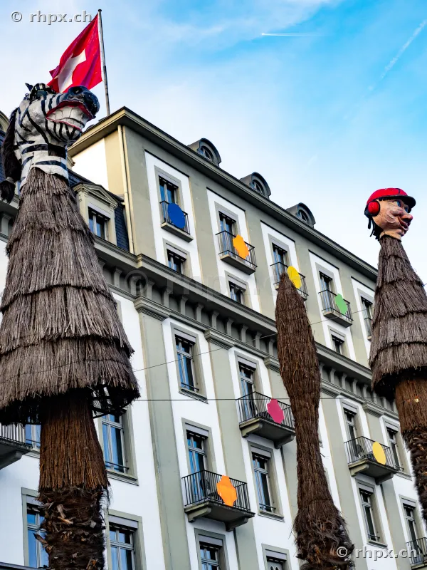 Fasnachtsdekoration in Form von hohen Strohfiguren vor der Fassade des Hotel Schweizerhof in Luzern