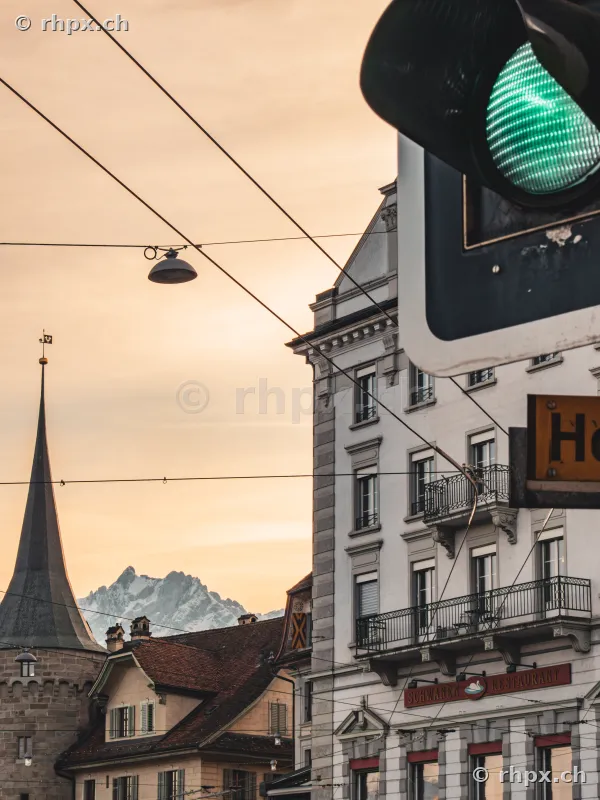 Green traffic light in the foreground with a tower and snow-capped mountains in the background in Lucerne
