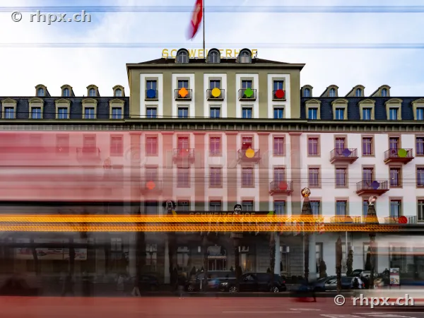 Fassade des Hotels Schweizerhof in Luzern mit einem durch Langzeitbelichtung unscharf dargestellten roten Bus im Vordergrund