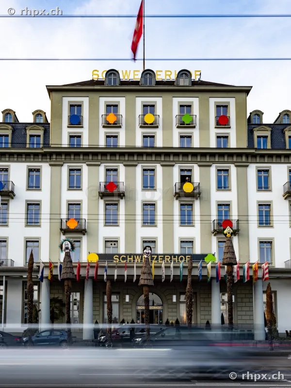 Fassade des Hotel Schweizerhof in Luzern mit bunten Dekorationselementen und vorbeifahrenden Autos bei Tageslicht