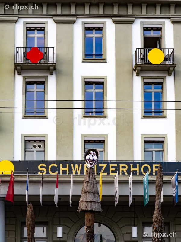 Fasnachtsmaske auf einem Pfahl vor der Fassade des Hotel Schweizerhof in Luzern