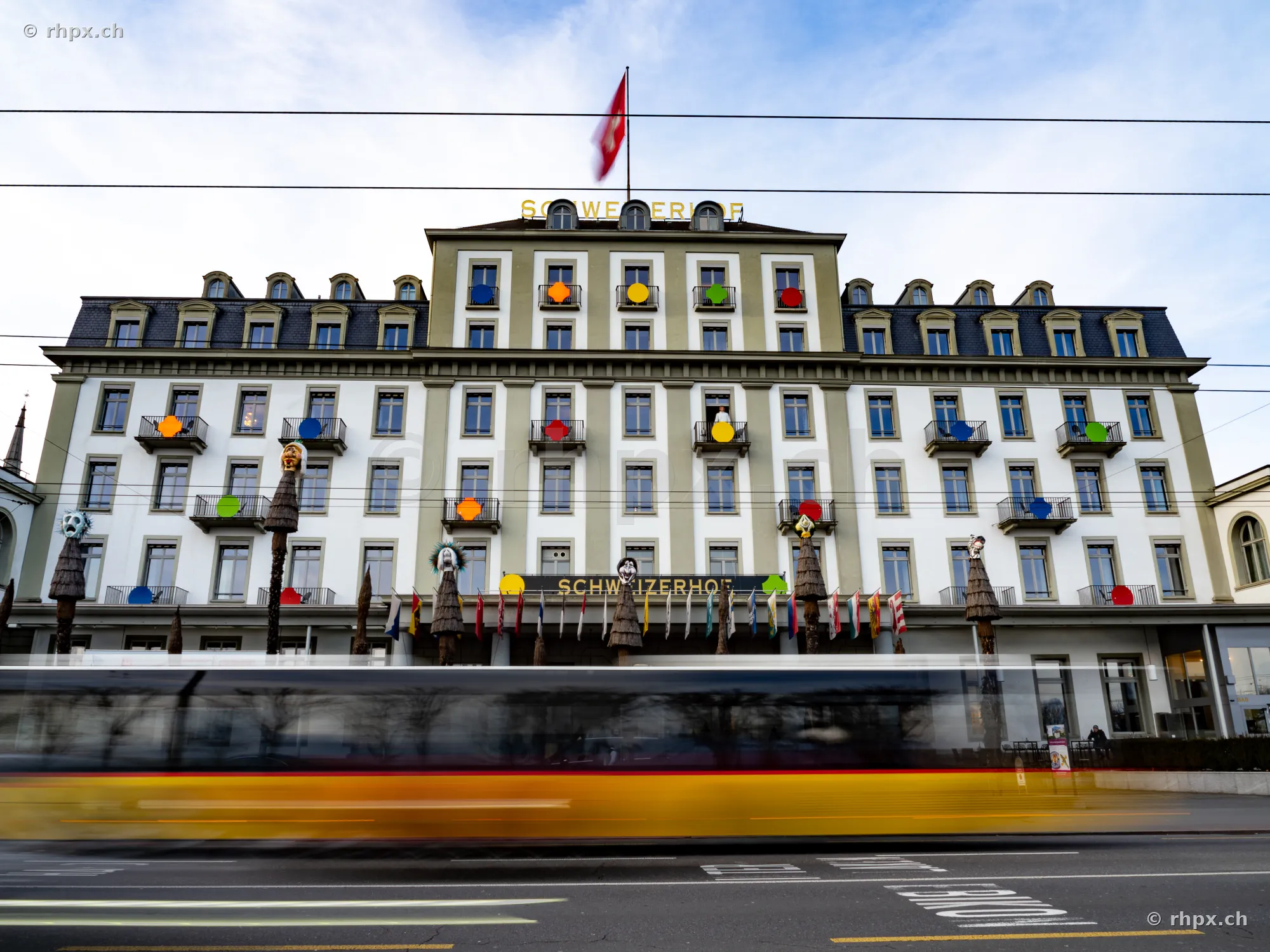 Hotel Schweizerhof Lucerne with colorful decorations on the facade and a passing bus in the foreground