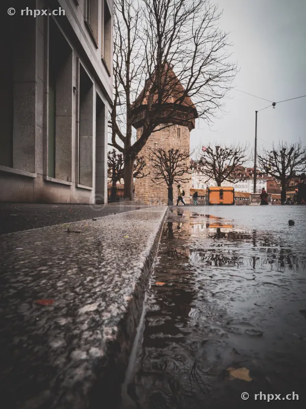 View of the Lucerne Wasserturm from ground level with reflection in a puddle