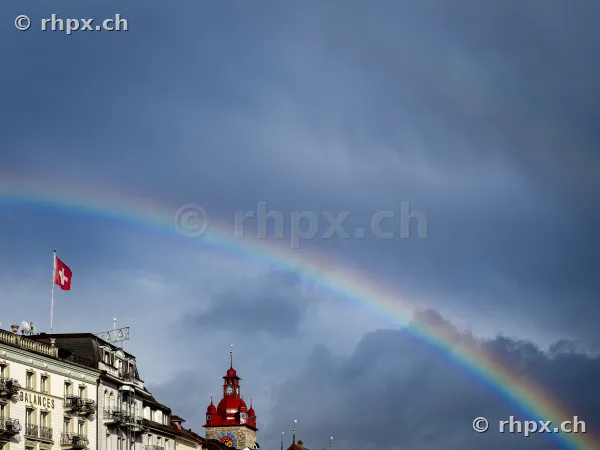 A rainbow stretches over the rooftops of the Lucerne Old Town with a Swiss flag.