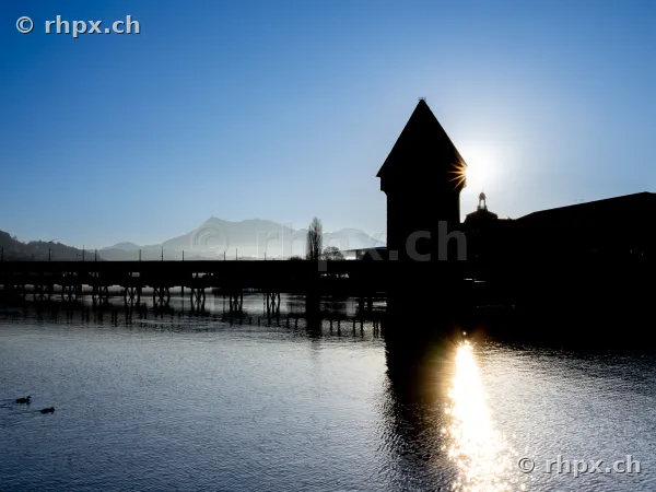 Silhouette of the Chapel Bridge and Water Tower in Lucerne backlit with a view of Mount Pilatus