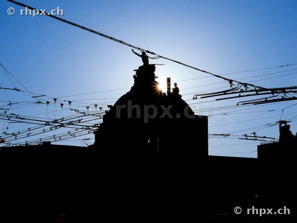 Backlit view of the sculpture on the dome of Lucerne railway station with overhead wires in the foreground