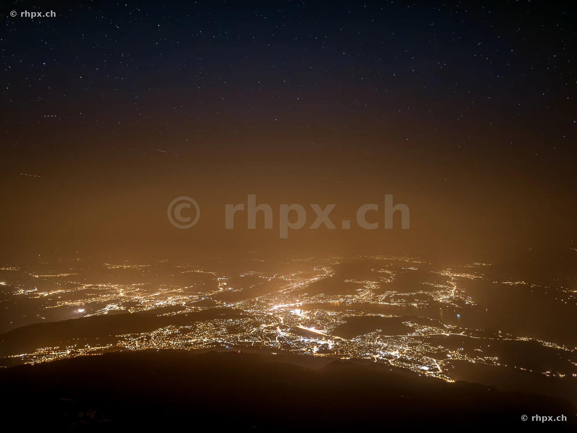 Nächtlicher Panoramablick vom Pilatus auf die beleuchtete Stadt und den Sternenhimmel