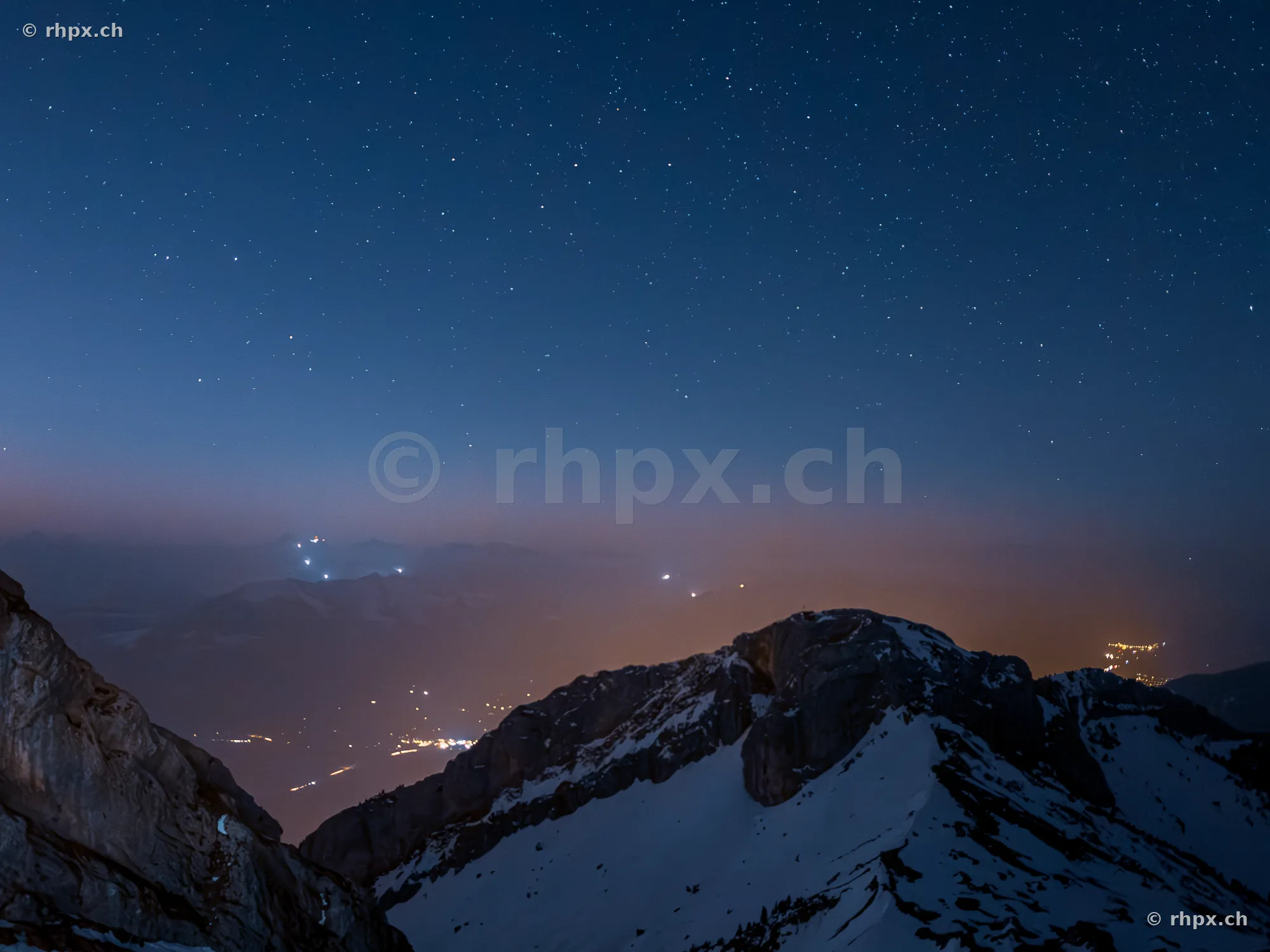 Snow-covered Mount Pilatus at night under a starry sky with valley lights