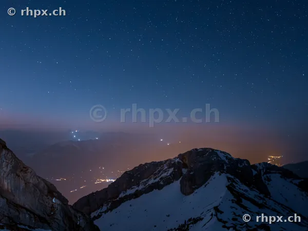 Snow-covered Mount Pilatus at night under a starry sky with valley lights