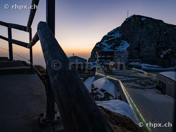View from a terrace towards the hotel buildings and the snow-covered rocky peak of Mount Pilatus at dusk