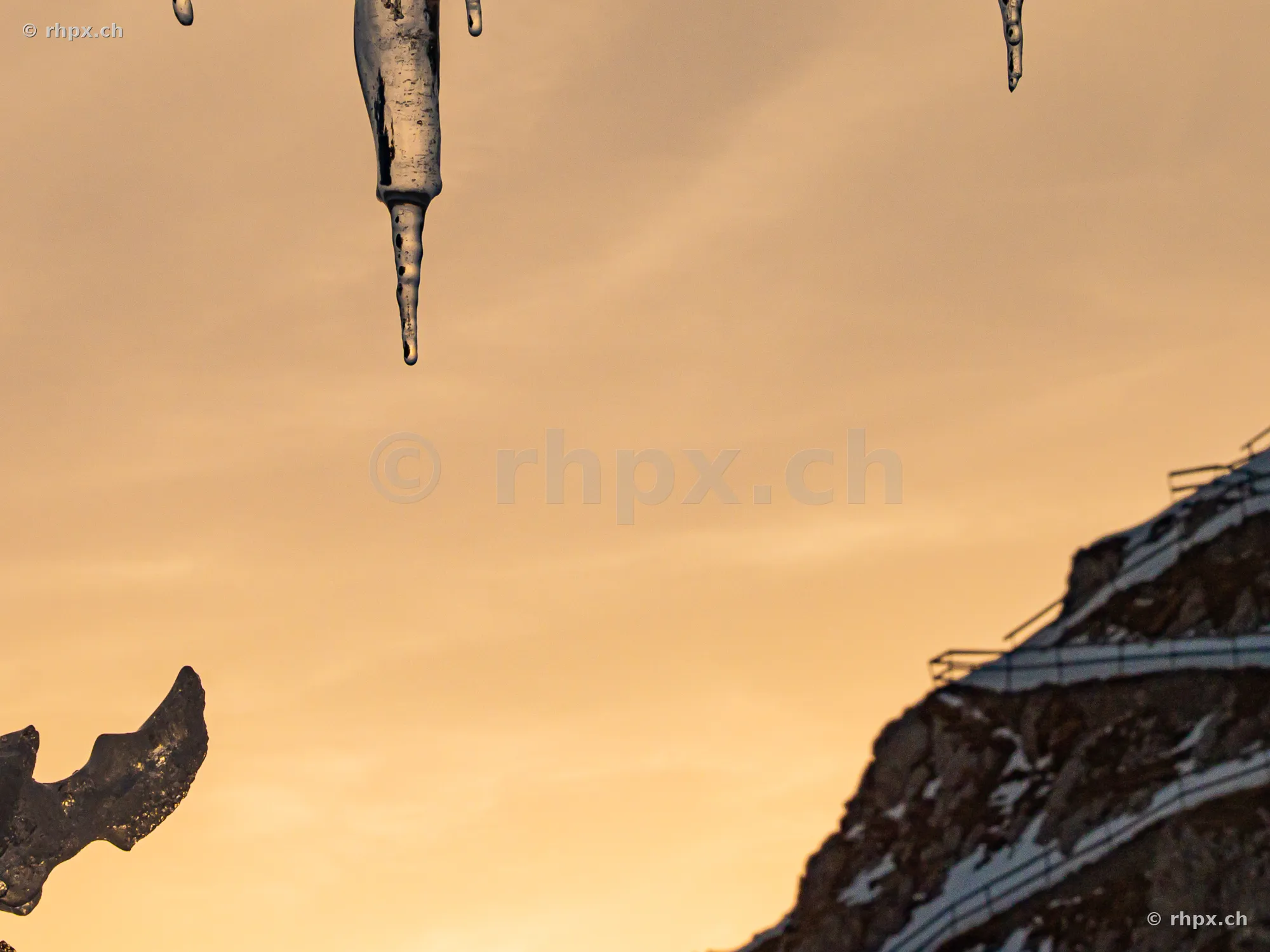 Icicles in the foreground with the snow-covered Mount Pilatus in the background during sunset.