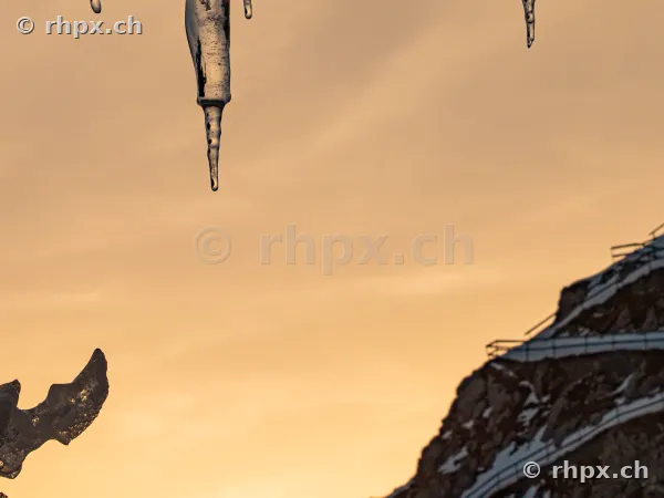 Icicles in the foreground with the snow-covered Mount Pilatus in the background during sunset.