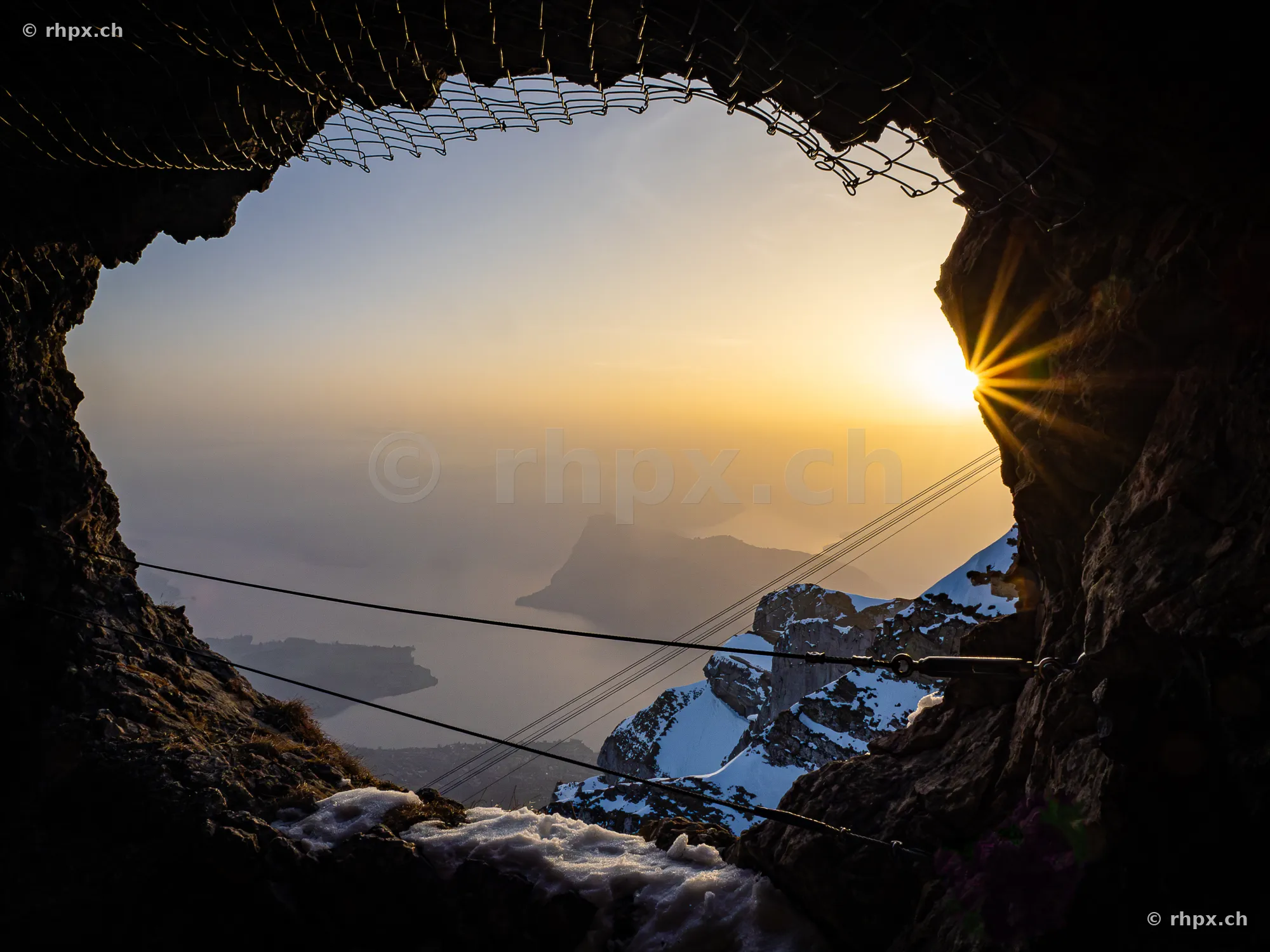View through a rock opening at Pilatus overlooking the snowy Alps and Lake Lucerne at sunset