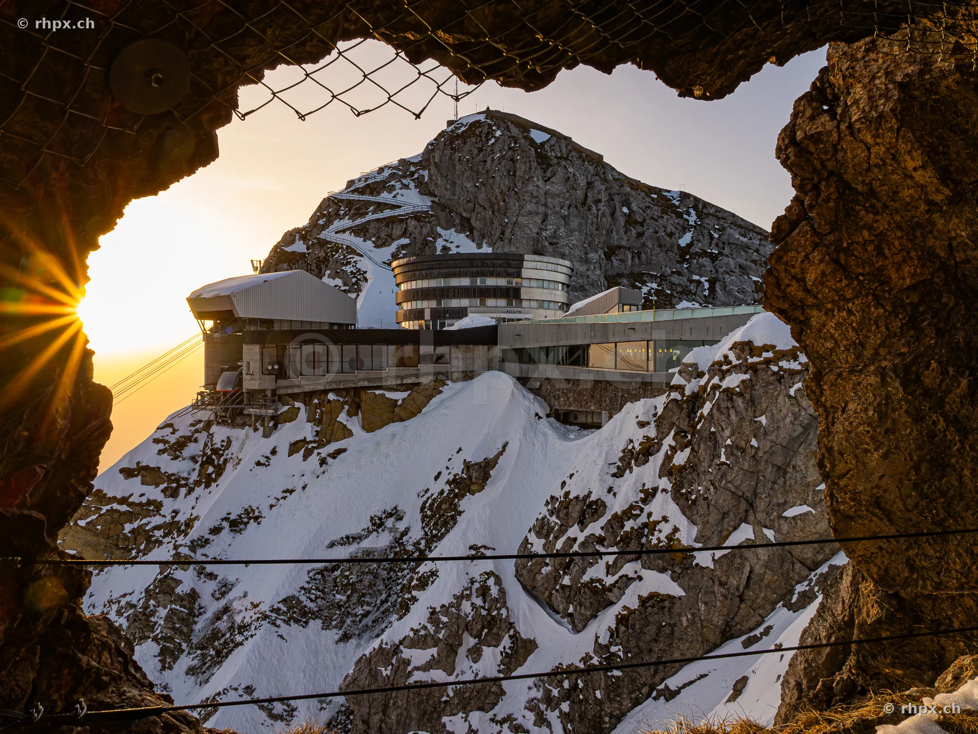 View through a rock opening of the Pilatus Kulm hotel and the snow-covered peak region.