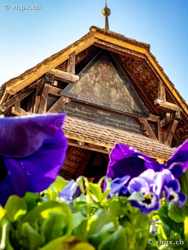 Close-up of a gable of the Chapel Bridge in Lucerne with blue flowers in the foreground
