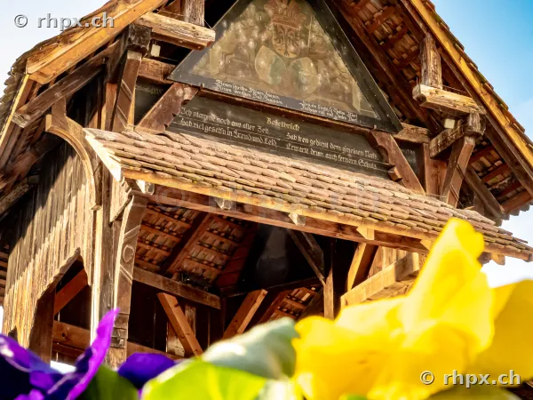 Close-up of a chapel bridge gable in Lucerne with coat of arms and inscription behind flowers