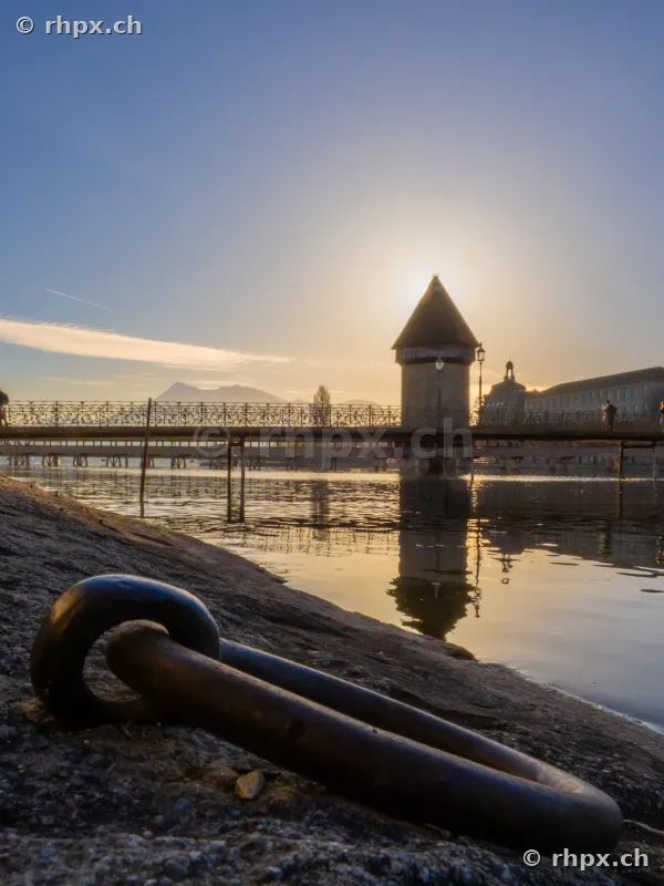 Water Tower and Chapel Bridge on Lake Lucerne at sunset with an iron mooring ring in the foreground.