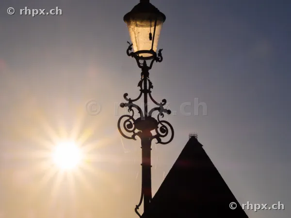 Silhouette of a historic street lamp against the setting sun in Lucerne