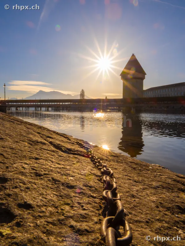Embankment wall with iron chain and view of the Chapel Bridge in Lucerne at sunset