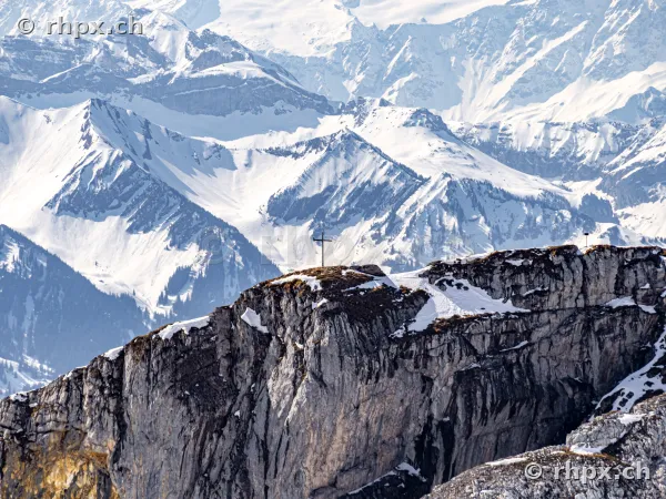 Summit cross on a rocky edge of Mount Pilatus in front of snowy mountain panorama