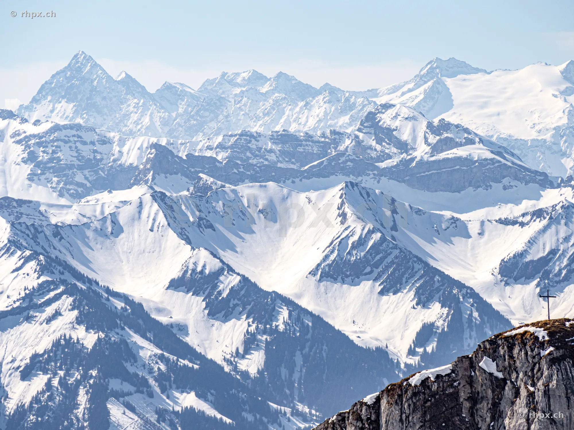View across snow-covered mountain peaks and the summit cross on Mount Pilatus