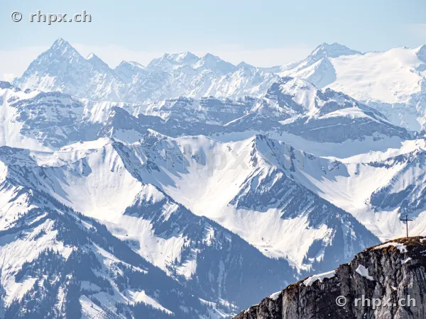 View across snow-covered mountain peaks and the summit cross on Mount Pilatus