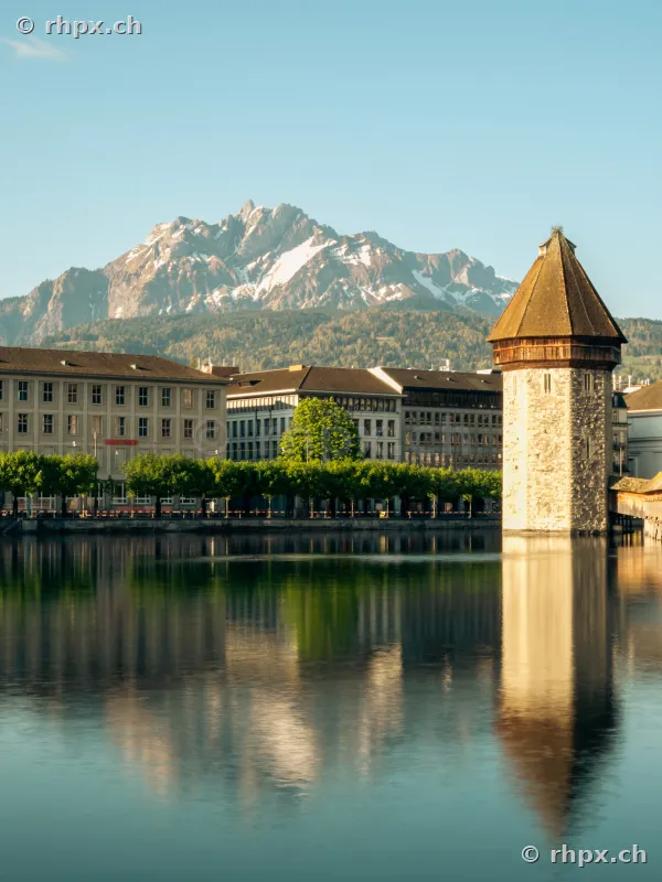Der historische Wasserturm in Luzern mit Spiegelung im Wasser und dem Pilatus im Hintergrund.