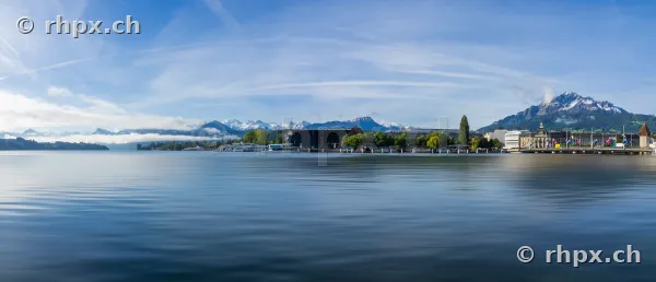 Wide angle view of Lake Lucerne with the city skyline and Mount Pilatus in the background under a blue sky.