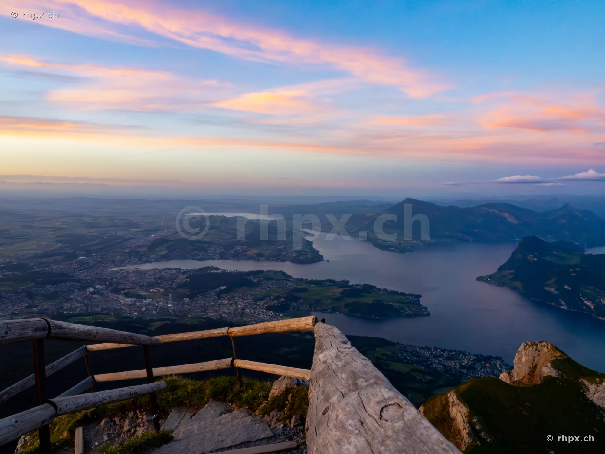 Wooden railing on Mount Pilatus overlooking Lake Lucerne and Central Switzerland at sunset.
