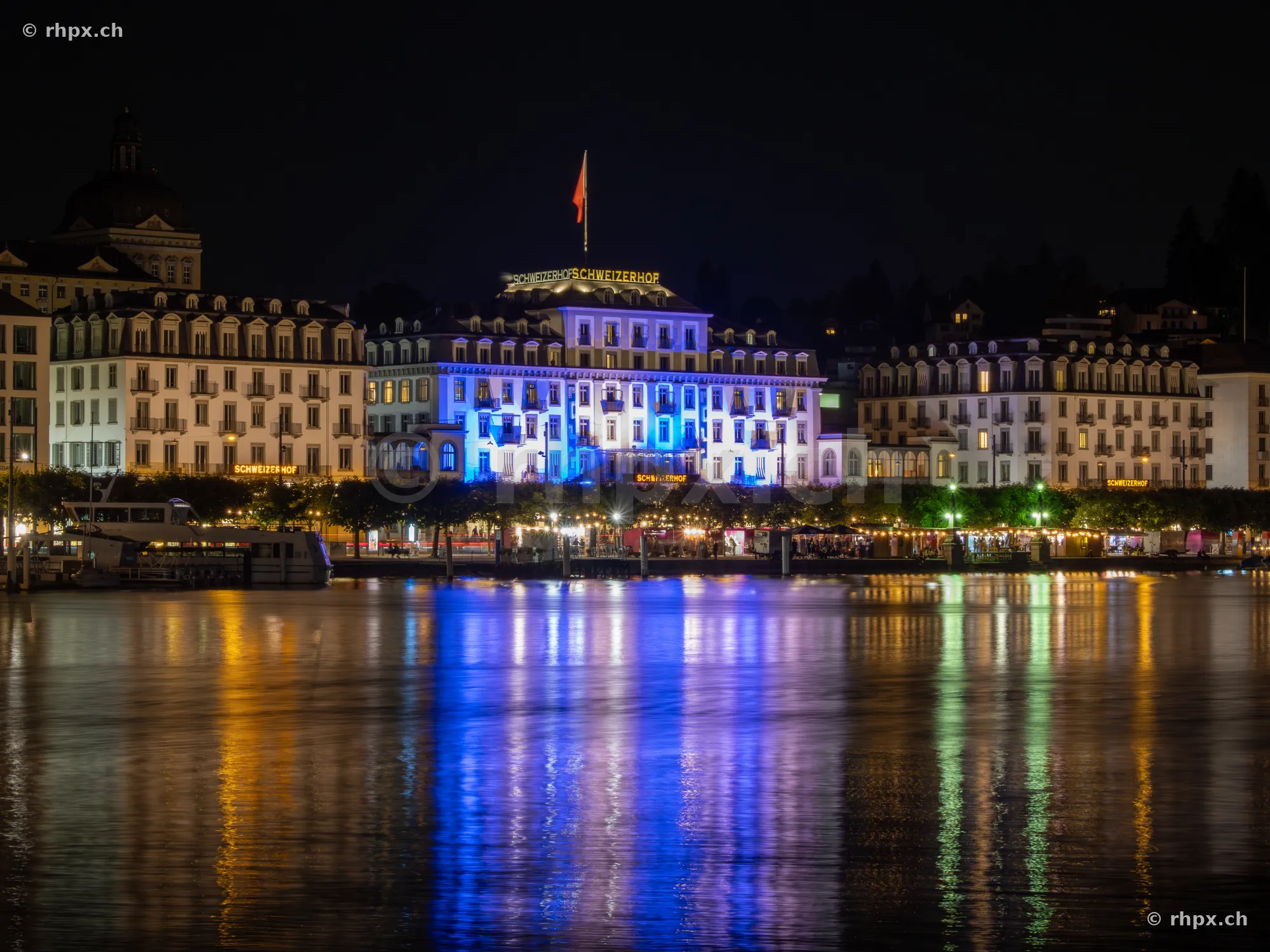 Illuminated facade of the Hotel Schweizerhof Lucerne on the shore of Lake Lucerne at night