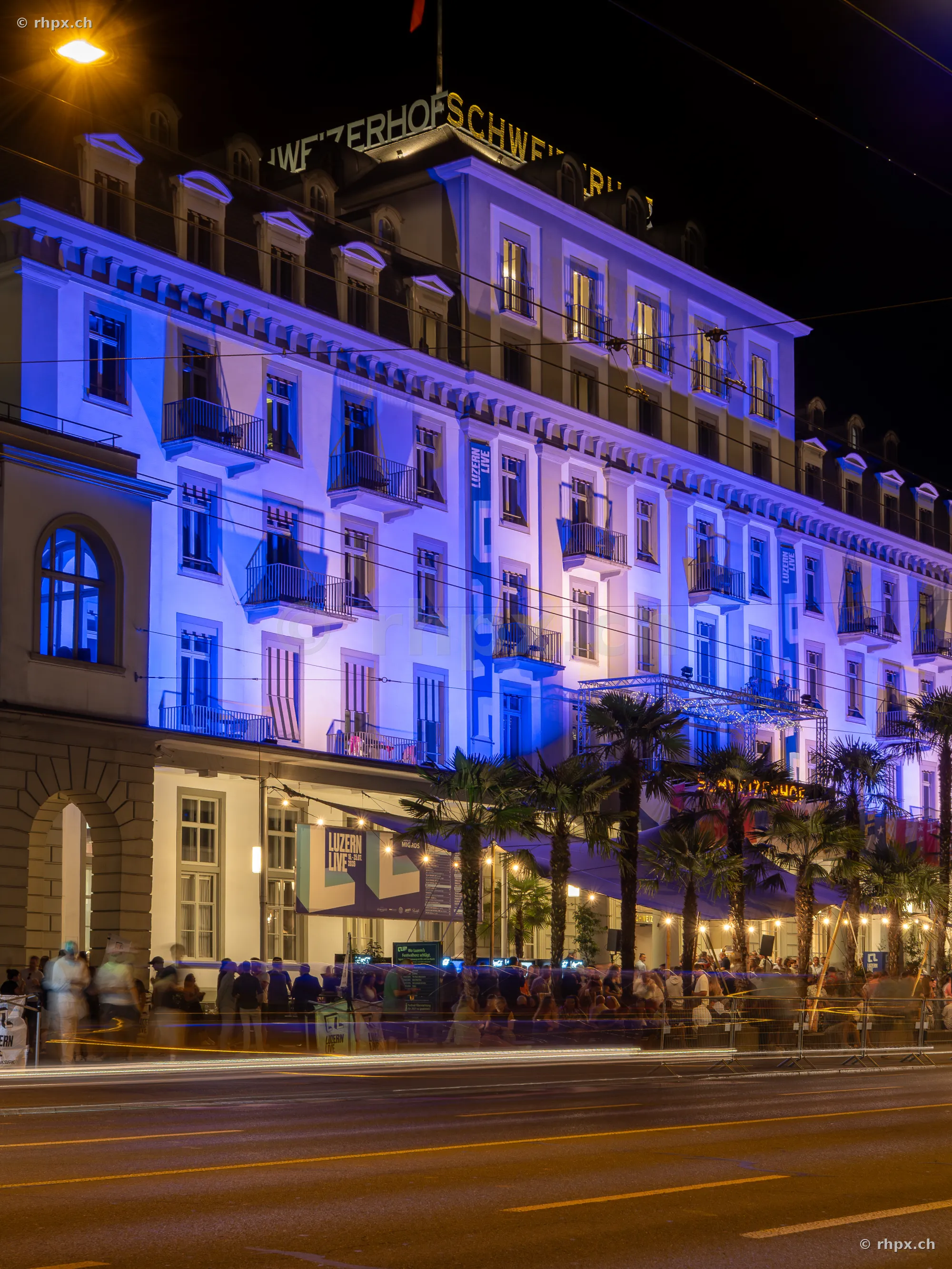Illuminated facade of the Hotel Schweizerhof in Lucerne at night with people in front of the building