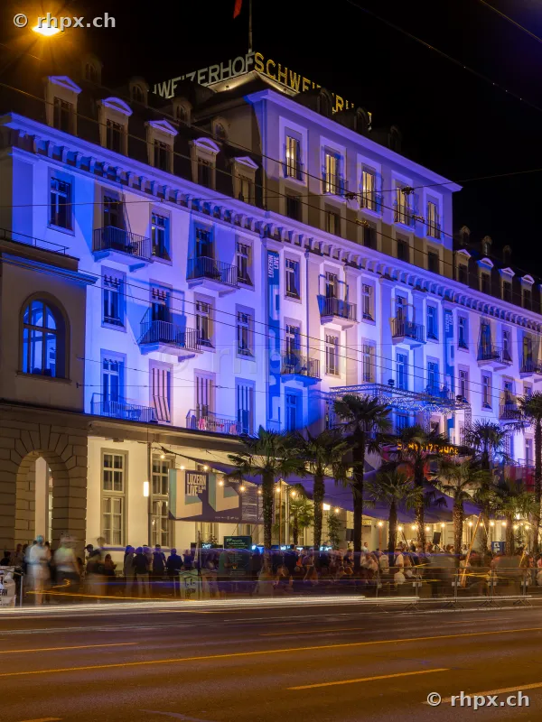 Beleuchtete Fassade des Hotels Schweizerhof in Luzern bei Nacht mit Personen vor dem Gebäude