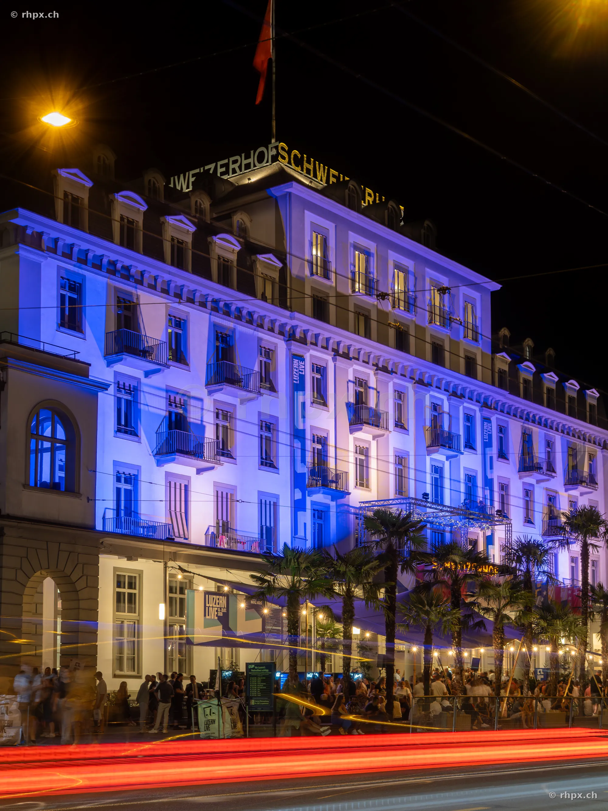 Hotel Schweizerhof Luzern in blauer Nachtbeleuchtung mit Festivalbesuchern vor dem Gebäude