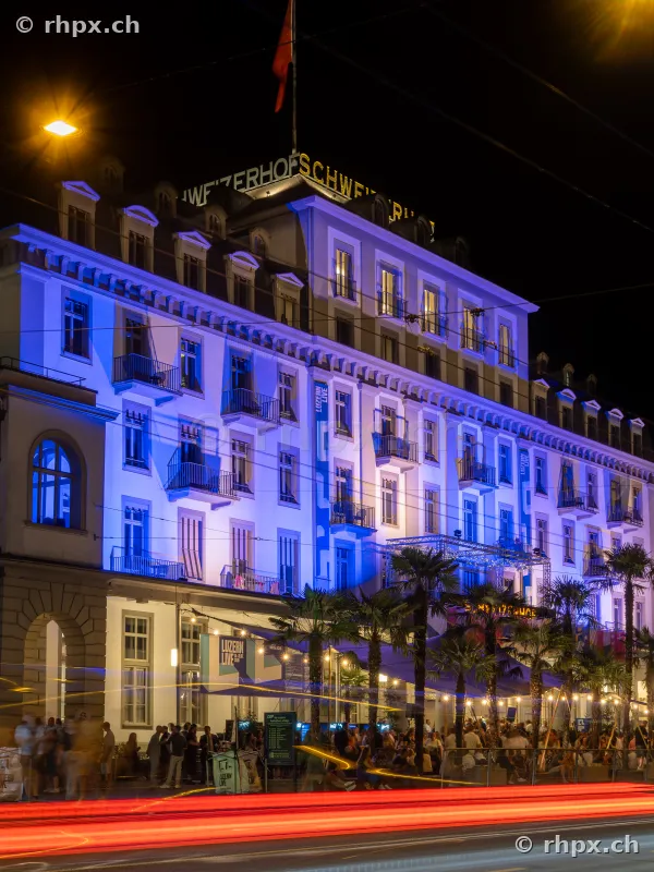 Hotel Schweizerhof Luzern in blauer Nachtbeleuchtung mit Festivalbesuchern vor dem Gebäude